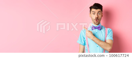 Check it out. Amazed caucasian man with moustache, wearing bow-tie, saying wow and pointing left, showing advertisement, standing on pink background 100617724