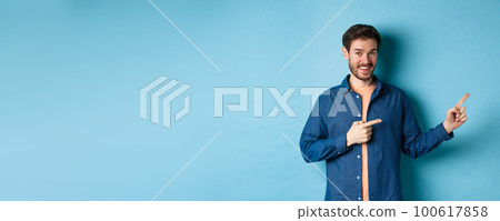 Cheerful caucasian man with beard pointing fingers aside at empty space and smiling at camera, showing advertisement, blue background Cheerful caucasian man with beard pointing fingers aside at empty space and smiling at camera, showing advertisement, blue background 100617858