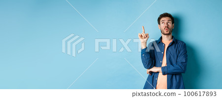Image of handsome man pitching an idea, raising finger and looking up thinking, standing on blue background Image of handsome man pitching an idea, raising finger and looking up thinking, standing on blue background 100617893
