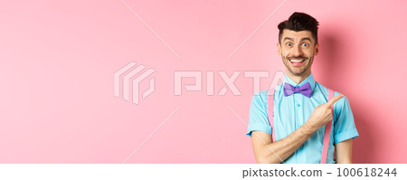 Handsome caucasian guy with bristle and moustache pointing finger right aside, showing advertisement, standing over pink background in classy bow-tie 100618244