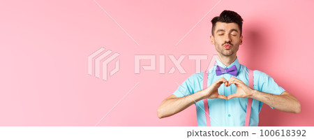 Happy Valentines day. Romantic boyfriend close eyes for kiss and showing heart, having date with lover, standing over pink background 100618392