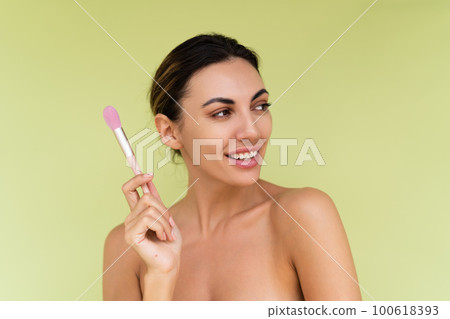 Beauty portrait of young topless woman with bare shoulders on green background with perfect skin and natural makeup holds blush brush Beauty portrait of young topless woman with bare shoulders on green background with perfect skin and natural makeup holds blush brush 100618393
