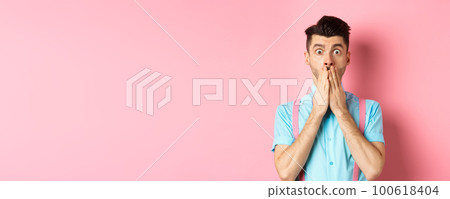 Shocked man looking in startled, covering mouth with hands and staring at camera, standing on pink background Shocked man looking in startled, covering mouth with hands and staring at camera, standing on pink background 100618404