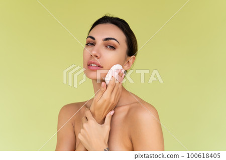 Beauty portrait of young woman with bare shoulders on green background with cosmetic powder puff velour makeup foundation blender sponge applicator 100618405