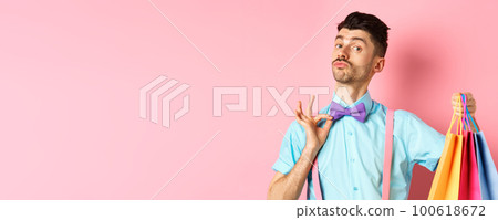 Fancy guy with moustache fixing his bow-tie and holding shopping bags, boyfriend bring gift packages, standing over pink background Fancy guy with moustache fixing his bow-tie and holding shopping bags, boyfriend bring gift packages, standing over pink background 100618672