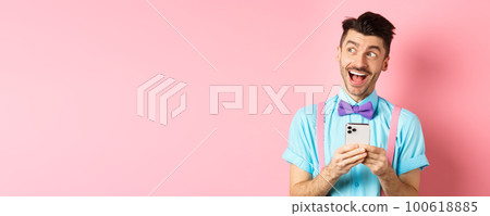 Technology concept. Excited man looking aside with dreamy face, winning online prize on smartphone, standing cheerful over pink background Technology concept. Excited man looking aside with dreamy face, winning online prize on smartphone, standing cheerful over pink background 100618885