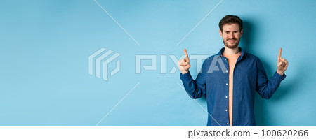 Skeptical young man frowning and squinting, cringe from something disgusting, standing on blue background 100620266