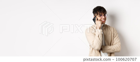 Real people concept. Handsome modern man talking on mobile phone, look aside and holding smartphone near ear, standing on white background 100620707