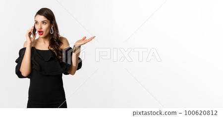 Attractive glamour woman in black dress talking on mobile phone, having conversation and looking surprised, standing over white background Attractive glamour woman in black dress talking on mobile phone, having conversation and looking surprised, standing over white background 100620812