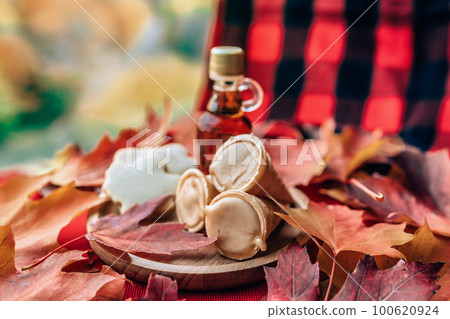 Maple syrup taffy cones dessert with traditional bottle and plaid cloth table - red leaves on table. Quebec local food. Maple syrup taffy cones dessert with traditional bottle and plaid cloth table - red leaves on table. Quebec local food. 100620924