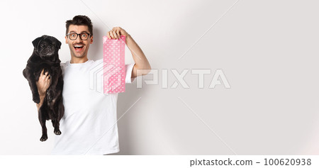 Image of hipster guy pet owner, holding cute black pug and dog poop bag, standing over white background Image of hipster guy pet owner, holding cute black pug and dog poop bag, standing over white background 100620938