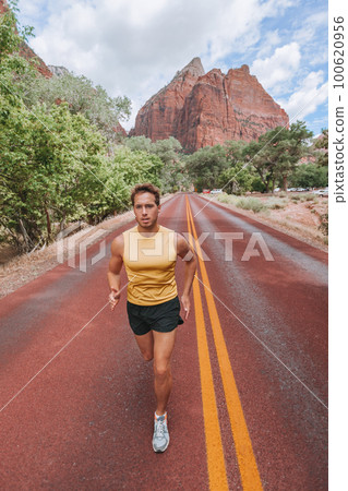 Athlete runner running on outdoor run jogging on red road outside in nature landscape. Vertical portrait of fit healthy young man training cardio for marathon or triathlon. Athlete runner running on outdoor run jogging on red road outside in nature landscape. Vertical portrait of fit healthy young man training cardio for marathon or triathlon. 100620956