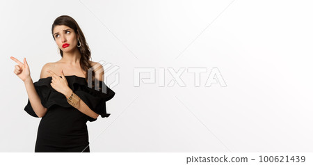 Fashion and beauty. Jealous glamour woman in black dress looking and pointing fingers left, sulking disappointed, white background Fashion and beauty. Jealous glamour woman in black dress looking and pointing fingers left, sulking disappointed, white background 100621439