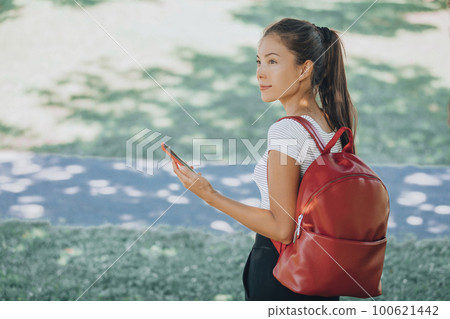 Asian student woman using mobile phone app online walking in college campus looking away up happy. Smartphone for coronavirus vaccine passport. Asian student woman using mobile phone app online walking in college campus looking away up happy. Smartphone for coronavirus vaccine passport. 100621442