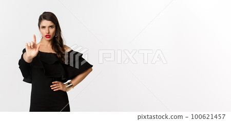 Fashion and beauty. Confident and serious lady in black dress, showing finger in stop gesture, prohibit and disapprove something, standing over white background 100621457