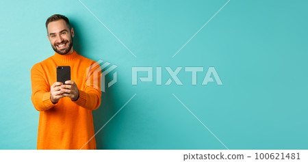 Happy handsome man taking photo on mobile phone, take pictures with smartphone camera, standing over light blue background Happy handsome man taking photo on mobile phone, take pictures with smartphone camera, standing over light blue background 100621481