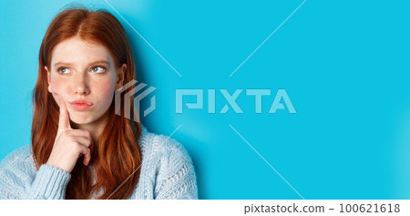 Headshot of troubled teenage girl thinking, looking bothered and frowning, standing against blue background 100621618
