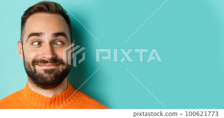 Headshot of funny caucasian man making faces, squinting and smiling silly, standing over light blue background 100621773