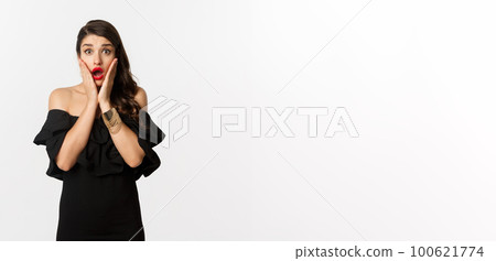 Beauty and fashion concept. Waist-up shot of surprised woman in black cocktail dress, looking amazed at camera, open mouth fascinated, standing over white background Beauty and fashion concept. Waist-up shot of surprised woman in black cocktail dress, looking amazed at camera, open mouth fascinated, standing over white background 100621774