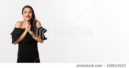 Fashion and beauty. Pretty woman in black dress asking for help, showing thank you gesture, looking grateful at camera, standing over white background Fashion and beauty. Pretty woman in black dress asking for help, showing thank you gesture, looking grateful at camera, standing over white background 100623025
