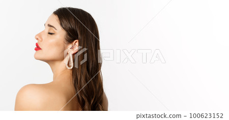 Fashion and beauty concept. Profile of beautiful woman standing naked with makeup and earrings, looking tender and sensual, standing over white background 100623152