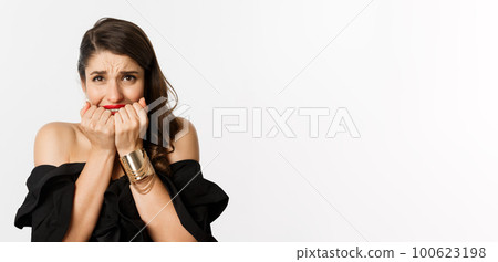 Fashion and beauty concept. Nervous woman looking concerned, biting fingernails and standing over white background 100623198