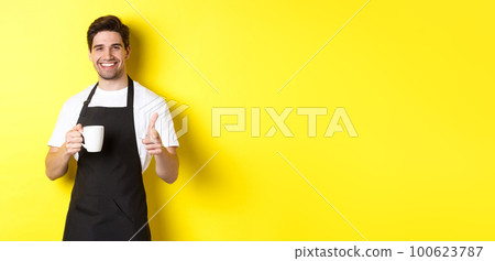 Barista bringing coffee and pointing finger gun at camera, standing in black apron against yellow background Barista bringing coffee and pointing finger gun at camera, standing in black apron against yellow background 100623787