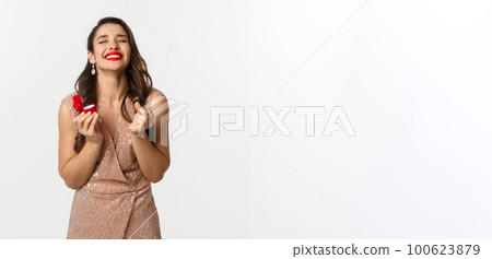 Satisfied and happy woman holding engagement ring and red small box, receive marriage proposal on new year eve, wearing elegant dress, smiling delighted, white background Satisfied and happy woman holding engagement ring and red small box, receive marriage proposal on new year eve, wearing elegant dress, smiling delighted, white background 100623879