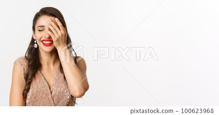 Concept of New Year celebration and winter holidays. Fabulous woman with red lips, wearing party dress, laughing and looking delighted, standing over white background 100623968