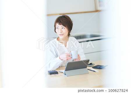 A woman taking a break with a mug while working from home A woman taking a break with a mug while working from home 100627824