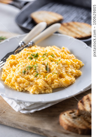 Tasty yellow freshly-made scrambled eggs with chives in a plate, served with toasted bread slices 100629805