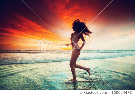 Woman running on the beach at sunset 100634478