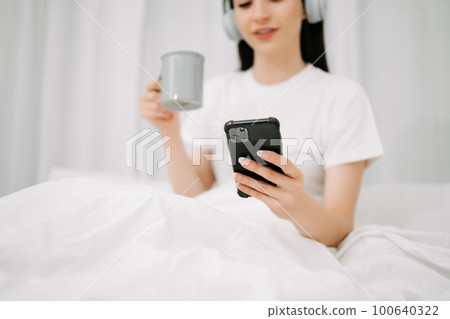 Beautiful woman has woken up on a white bed and holding coffee in the morning at home in morning Beautiful woman has woken up on a white bed and holding coffee in the morning at home in morning 100640322