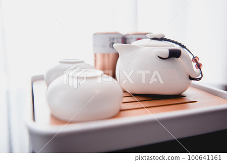 Still life details in home interior of living room. Sweaters and cup of tea with steam on a serving tray on a coffee table. Breakfast over sofa in morning sunlight. Cozy autumn or winter concept Still life details in home interior of living room. Sweaters and cup of tea with steam on a serving tray on a coffee table. Breakfast over sofa in morning sunlight. Cozy autumn or winter concept 100641161
