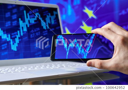 Trader analyzes stock market data in smartphone on the background of stock charts 100642952
