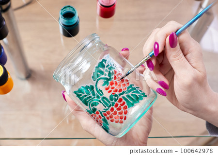 A girl paints a glass jar with stained glass paints A girl paints a glass jar with stained glass paints 100642978