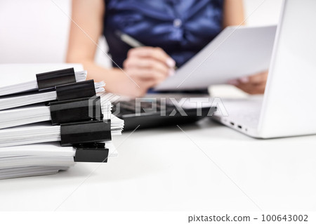 A stack of papers with Binder Clips against the background of an office worker working with documents 100643002