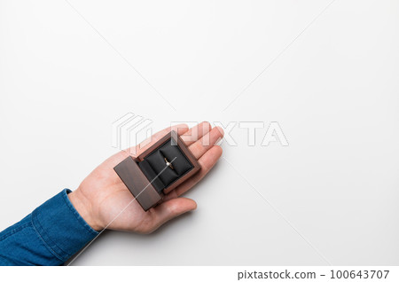 man makes a marriage proposal by presenting a ring in a wooden box. Close-up. View from above. A man's hand holds a gift box with a wedding ring on a white background. Place for text 100643707