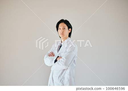 A young man in a white coat standing with his arms folded 100646596