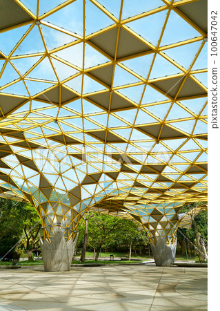 A futuristically designed sunshade with holes for trees in a city recreation park A futuristically designed sunshade with holes for trees in a city recreation park 100647042
