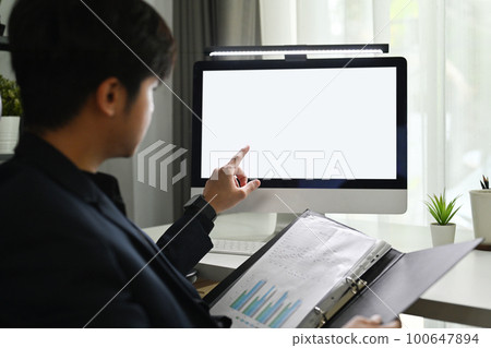 Back view of young man investor looking at computer monitor, analyzing project statistics or statistics data at workplace 100647894