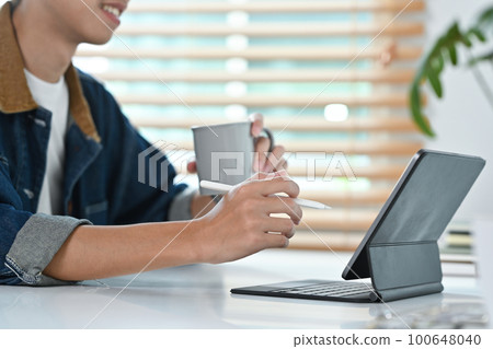 Young hipster man holding cup go coffee and working on design project on digital tablet at office Young hipster man holding cup go coffee and working on design project on digital tablet at office 100648040