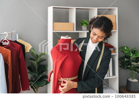 Female stylist Successful Fashion Business. Portrait of Smiling Black Designer stylish standing and working at fashion studio. Portrait of fashion designer in office. Female stylist Successful Fashion Business. Portrait of Smiling Black Designer stylish standing and working at fashion studio. Portrait of fashion designer in office. 100648385