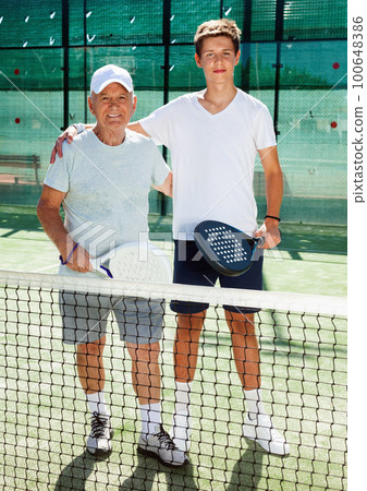senior man and young man posing on padel court senior man and young man posing on padel court 100648386