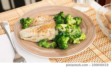 fried fillet of sea bass with garnish of broccoli on black warm stone plate 100648419