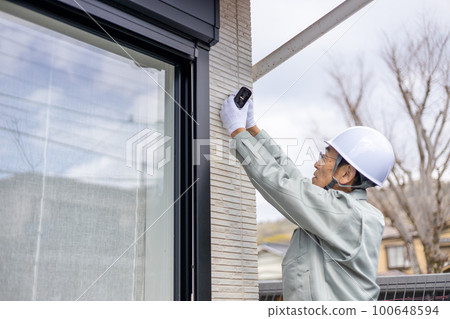 A male worker who installs a security camera on the wall of a detached house A male worker who installs a security camera on the wall of a detached house 100648594
