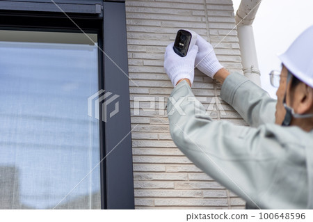 A male worker who installs a security camera on the wall of a detached house 100648596