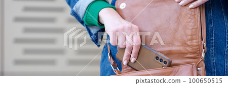 Young woman putting modern smartphone in bag Young woman putting modern smartphone in bag 100650515