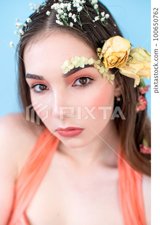 Cosmetics and manicure. Close-up portrait of attractive woman with dry flowers on her face and hair, pastel color, perfect make-up and skin on blue background. Fresh, trendy, spring retouched portrait Cosmetics and manicure. Close-up portrait of attractive woman with dry flowers on her face and hair, pastel color, perfect make-up and skin on blue background. Fresh, trendy, spring retouched portrait 100650762