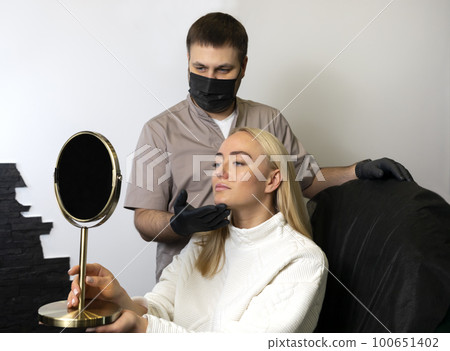 Doctor, beauty physician shows woman results of beauty injection procedure, face reshape with filler. White smiling happy female looks at mirror. Lifestyle, Aesthetic medicine. Horizontal plane Doctor, beauty physician shows woman results of beauty injection procedure, face reshape with filler. White smiling happy female looks at mirror. Lifestyle, Aesthetic medicine. Horizontal plane 100651402